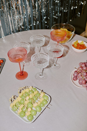 Table displaying empty crystal glasses, bowls of chips and salsa, skewers with green grapes and...