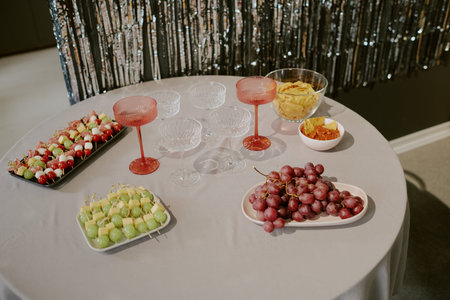Table displaying glassware, red and clear wine glasses, bowls of chips with salsa, skewered fruit...
