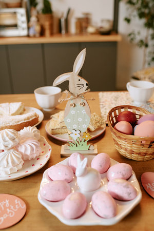 Easter table setting featuring wooden bunny figurine standing among pink dyed eggs, basket of...