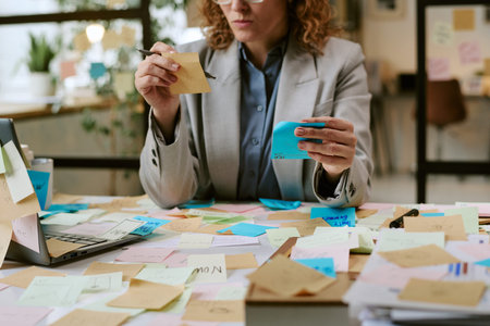 Caucasian woman sitting at desk organizing sticky notes and planning business tasks surrounded by...