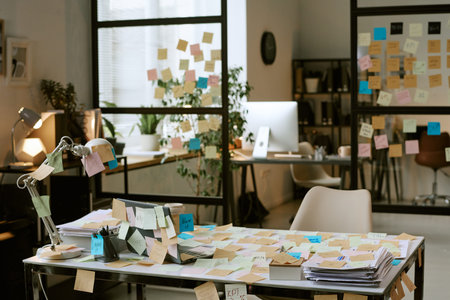 Modern office workspace covered with sticky notes on desk, glass walls, and computer monitor,...