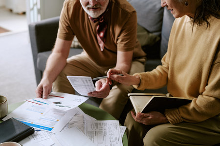 Senior Caucasian man and woman reviewing financial documents together at table, woman holding notebook and pen, man examining printed statementsの写真素材