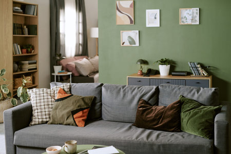 Modern living room featuring gray sofa with assorted pillows standing against green wall with framed...