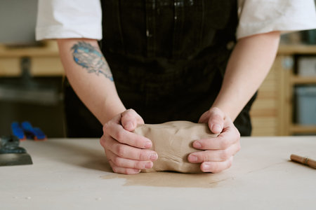 Caucasian young adult woman shaping clay with both hands on worktable, engaging in pottery or...