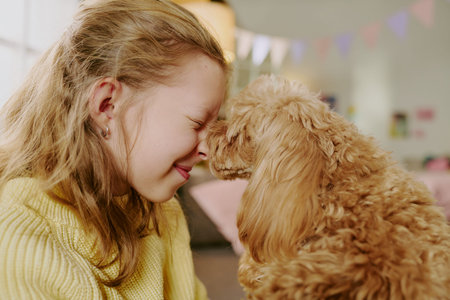 Caucasian girl child smiling with eyes closed touching nose to small fluffy dog indoors, showing...