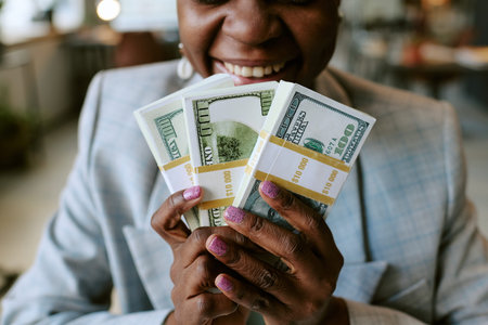 Black woman smiling while holding several stacks of US dollar bills in both hands, showing manicured...