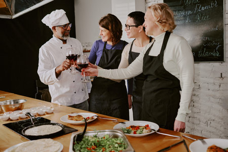 Group of middle aged multiethnic adults wearing aprons standing in cooking class kitchen clinking...