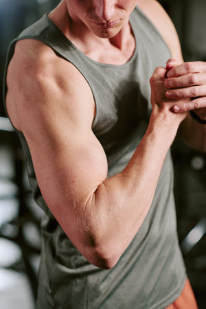 Vertical shot of young adult Caucasian man flexing arm muscles during gym workout, showing strength training progress and fitness discipline. Ideal for sports marketing and wellness ads