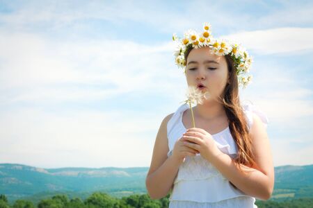 Girl blowing away dandelion seeds in the blue skyの写真素材