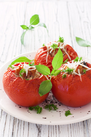 Baked tomatoes stuffed with mince and cheese on white plate over white wood backgroundの写真素材