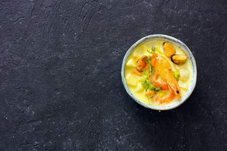 Soup with seafood, potatoes and cream over black atone background. Top view. Copy space