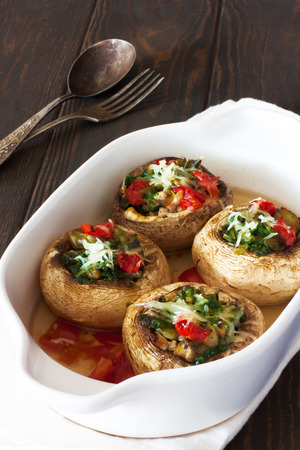 Mushrooms stuffed with vegetable mince and cheese in the white pot on a dark wood backgroundの写真素材