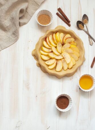 Homemade apple pie and bakery ingredients ( broun sugar, cinnamon and hohey) on a white wooden background. Flat lay. Copy spaceの写真素材