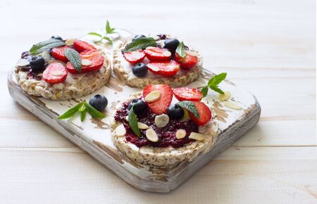 Open sandwiches with cream cheese, strawberries, blueberries, jam and almond flakes on the cutting...