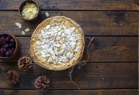 Grated rustic pie with ricotta, berries and almond flakes on dark wooden background. Flat lay