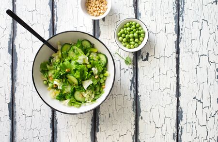 Mix salad leaves, cucumbers. pine nuts and green peas salad in white bowl on white painted table. Flat lay. Copy spaceの写真素材