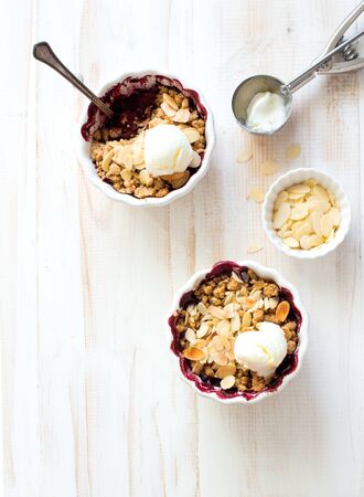 Crumble with berries, apples, ball of ice cream almond in white bowls close up on white wooden background. Flat lat. Copy spaceの写真素材