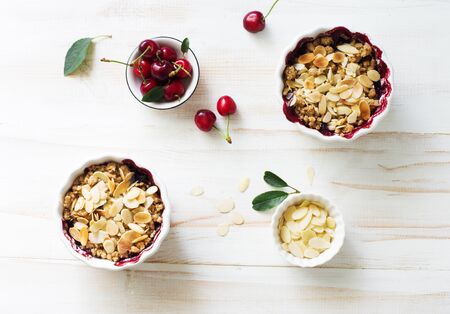 Crumble with berries, apples, and almond in white bowl on white wooden table close up. Flat lay. Copy spaceの写真素材