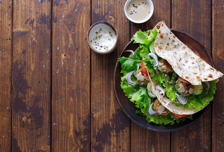 Pita bread with raw vegetables and falafel patties on dark wooden table close up. Flat lay. Copy spaceの写真素材