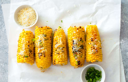 Ears of corn baked with herbs and parmesan cheese on white baking paper close up.Flat lat