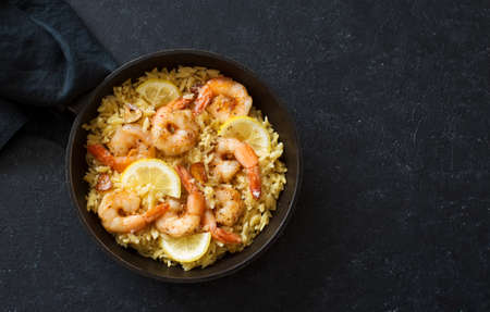 Orzo pasta with shrimps and lemon in a skillet on black stone background. Flat lay. Copy spaceの写真素材