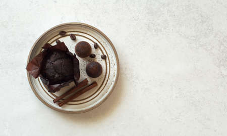 Chocolate muffin, candies and cinnamon sticks on brown plate on gray stone background. Flat lay....