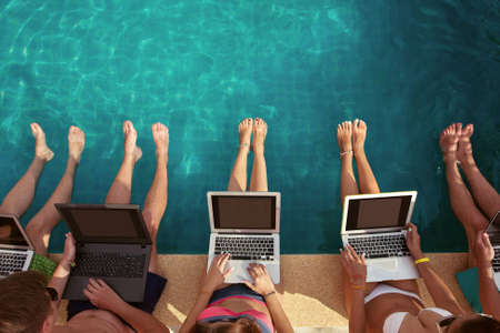 Group of people freelancers using laptop computer sitting near swimming pool and work togetherの写真素材