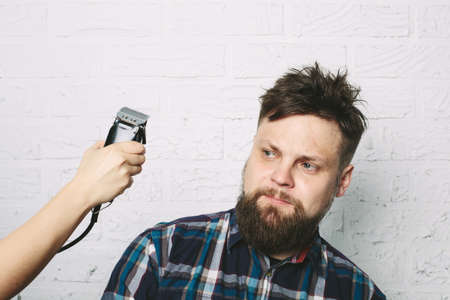 Funny hipster man with beard in hair salon. hairdresser hand with electric razorの写真素材