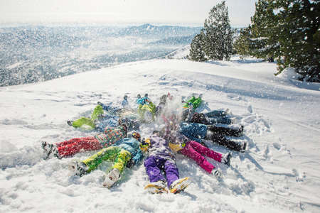 Laughing people lying on a snowy mountain top, merry winter holidays, winter sportsの写真素材