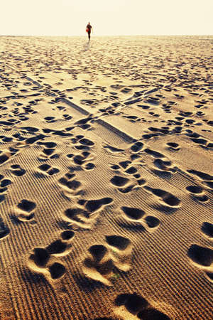 Steps on the sand, sunset, silhouette of person walking on sea beachの写真素材