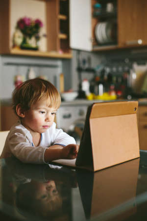 Little baby Girl sitting on kitchen with tablet pc using touchscreenの写真素材