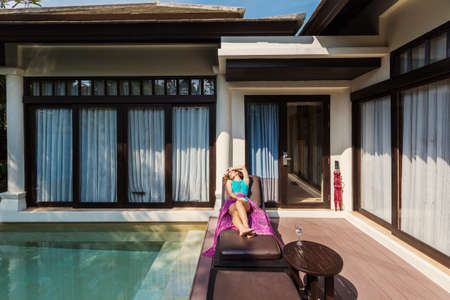 Woman lying on chaise lounge near pool luxury villa, have sunbathe, enjoying summer vacation