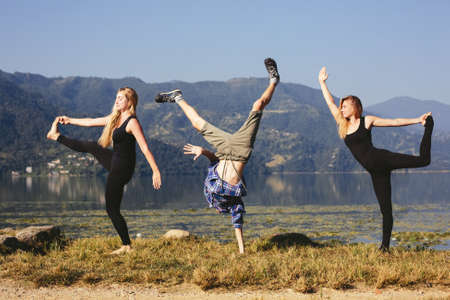 Happy funny yoga people try to doing fitness yoga exercises outdoor on beautiful mountain lake in...
