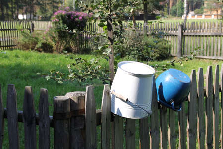 a blue cast iron pot and a white bucket hanging on the wooden fence of a farmhouseの写真素材