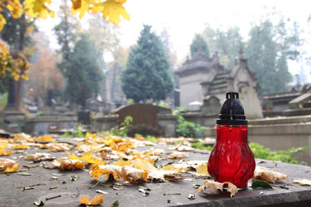 a red candle on the surface of an old tomb with autumn leaves around and other tombsの写真素材