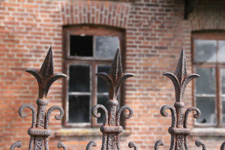 protruding pins of an old metal fence and behind them a blurred view of a brick building with broken...