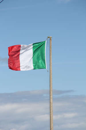 waving Italian flag against the sky hung on a cement poleの写真素材