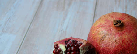 two pomegranates, red fruit, pomegranates on a light wooden background, an open pomegranate and juicy red pomegranate seedsの写真素材