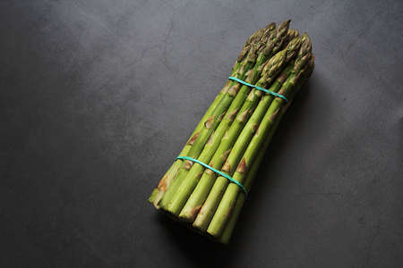 bunch of green asparagus, green vegetables, asparagus tied with a rubber band on a dark background, asparagus tips, vegetables full of vitaminsの写真素材