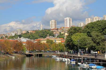 water canal in the city of Rijeka, bridge over the canal, small boats moored in a row, autumn trees and settlements on hills, high blocks above the city, Croatiaの写真素材