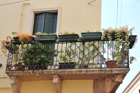 balcony on a typical Italian tenement house, old balcony decorated with pots of flowers, wooden shutters, metal balcony hoopの写真素材