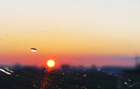 Sunset behind the raindrops on the window, view of the sunset through wet glass, rain on the glass, sun setting in the distance, raindrops, drops on the glassの写真素材