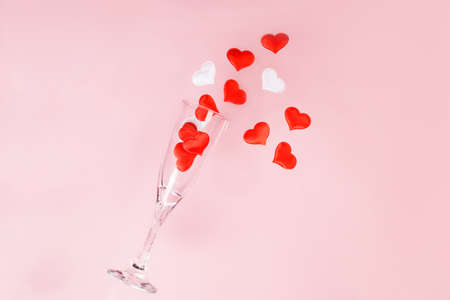 One glass of champagne with a splash of red and white heart shaped confetti on a pink background Valentines dayの写真素材