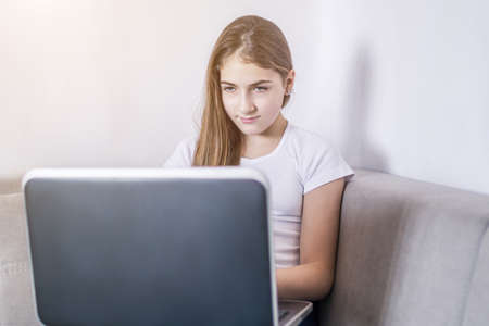 Young girl working on a notebook computer sitting on the bed. distance learning, self education in terms of quarantineの写真素材