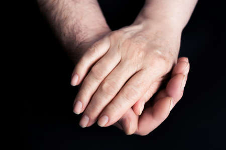 Hands of seniors men and women on a black paper background Hand of men touching senior women.の写真素材