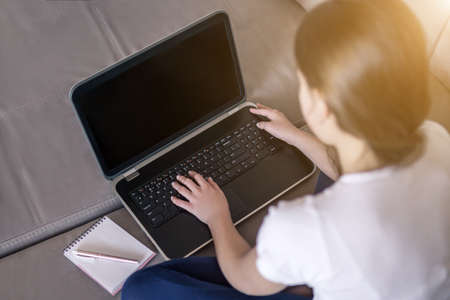 Young girl working on a notebook computer sitting on the bed in the house distance learning self education in terms of quarantineの写真素材