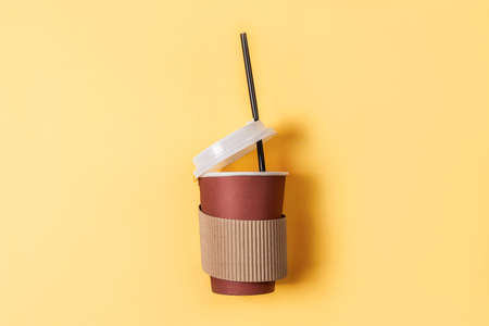 Disposable paper cup of coffee on a pastel yellow background. Flat lay style. Paper cup of coffeeの写真素材