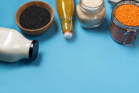 Variety of seeds of white and black sesame seeds of orange lentils in glass jars on a wooden plate a...
