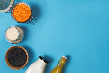 Variety of seeds of white and black sesame seeds of orange lentils in glass jars on a wooden plate a...