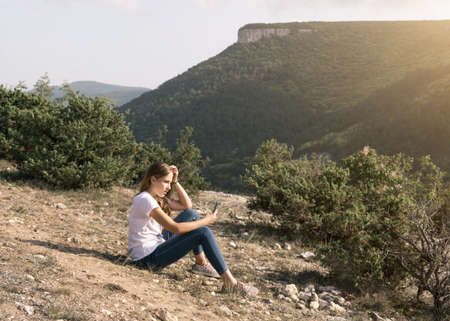 Beauty portrait of a young girl with long hair enjoying nature outdoors with a phone, beautiful warm sunlightの写真素材